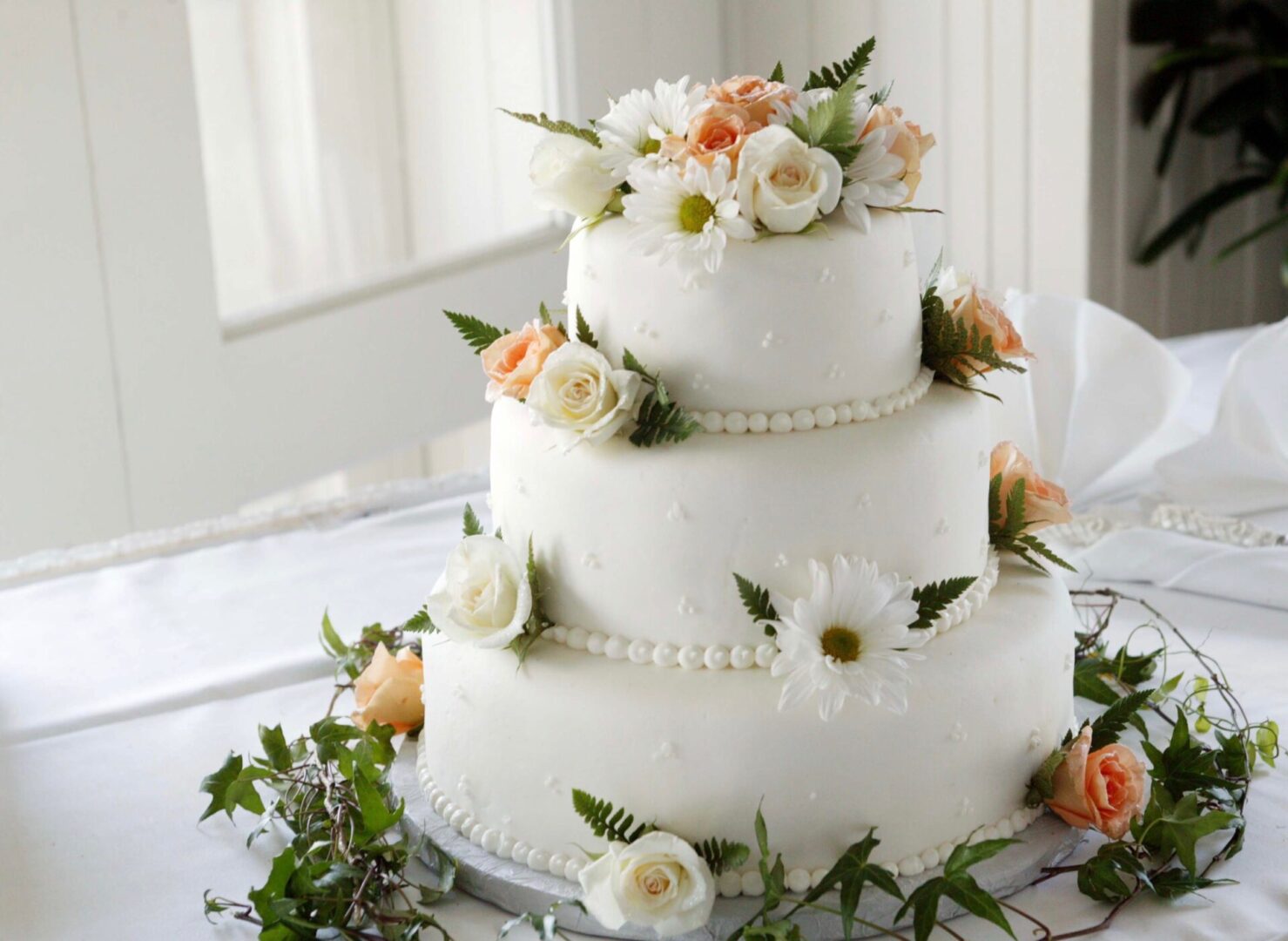 a three layered wedding cake with pearl and flowers decoration