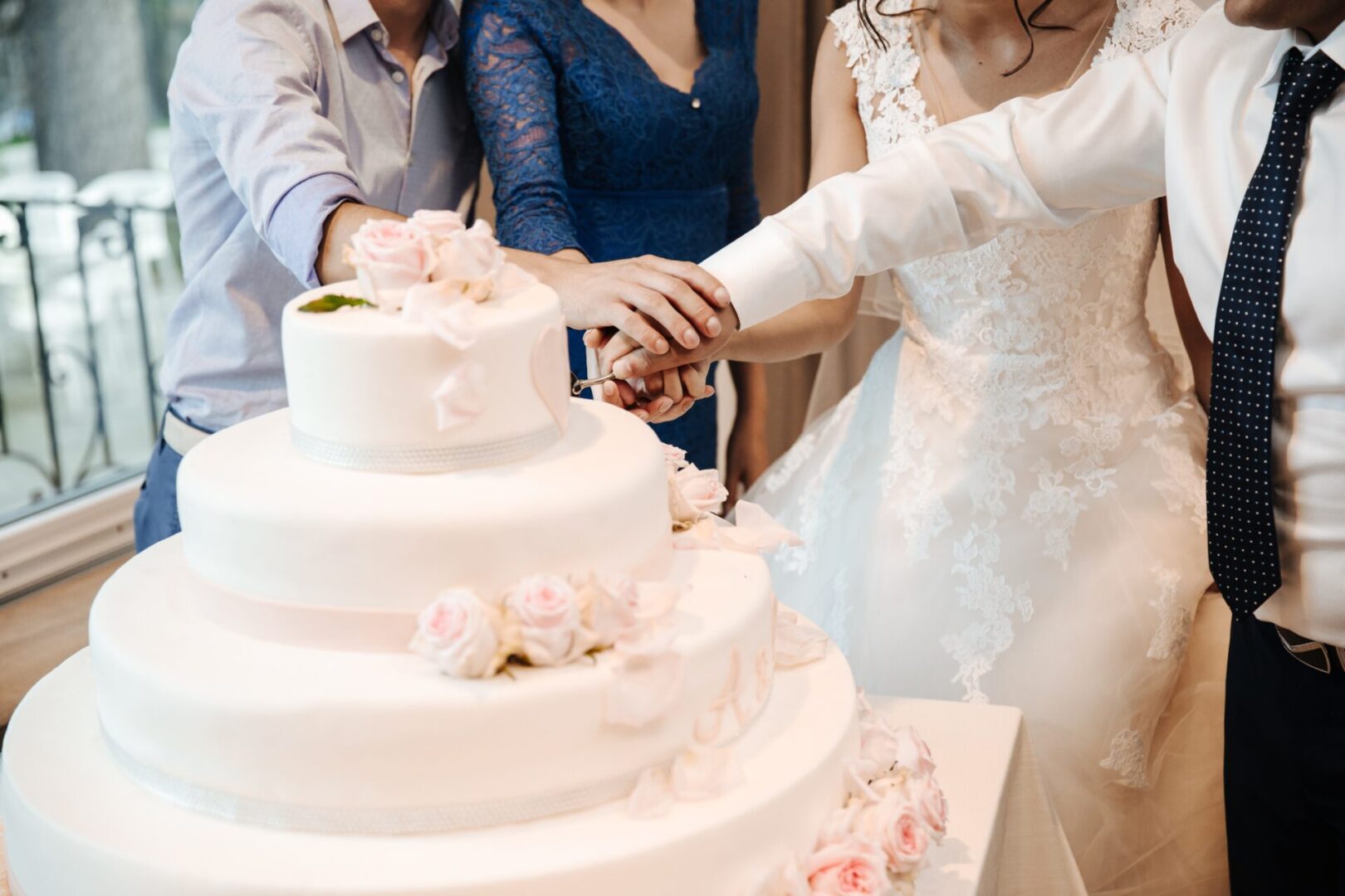 two people cutting a big cake with bride and groom
